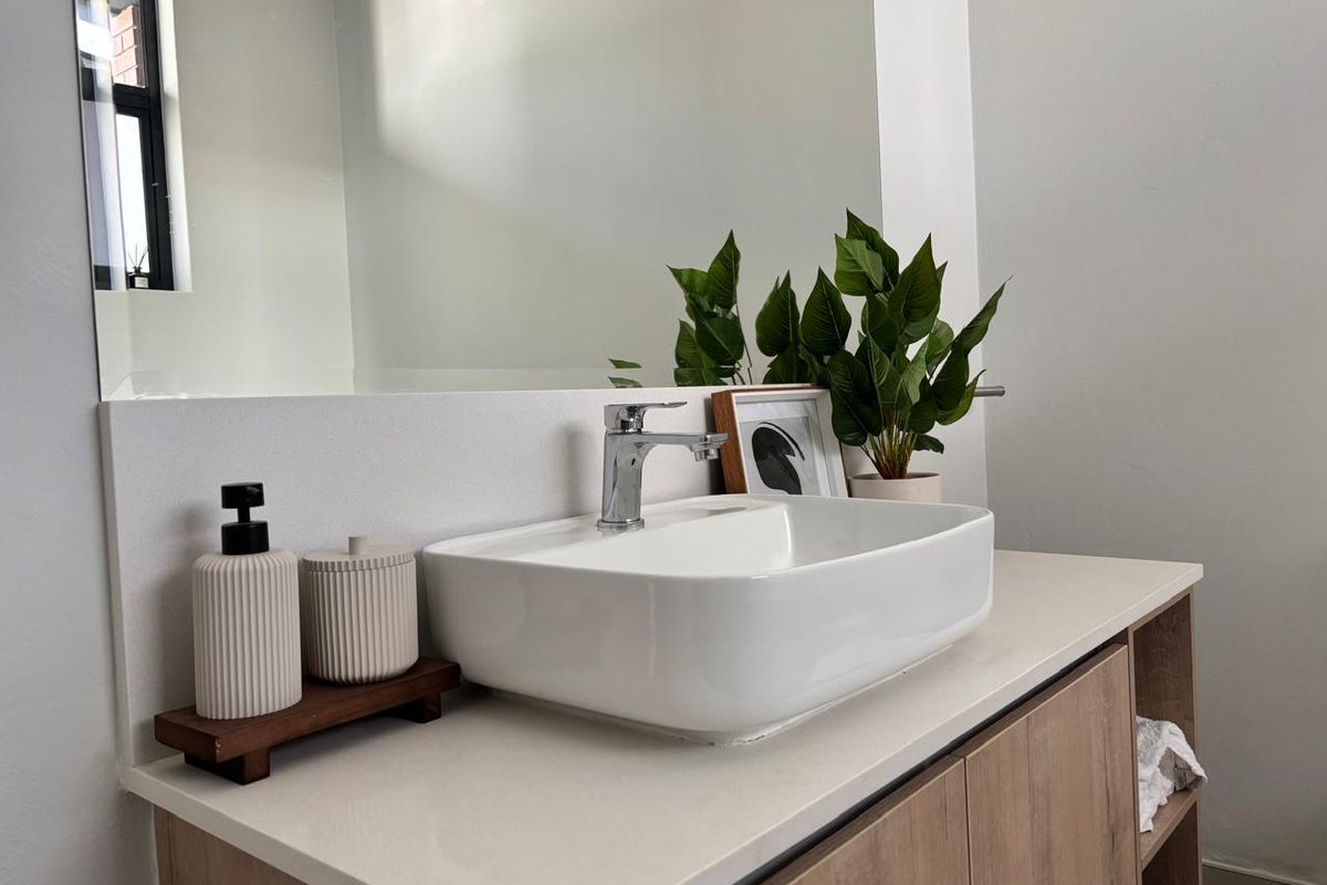 A modern bathroom vanity featuring a white vessel sink, chrome mixer tap, stone countertop, and a large wall-mounted mirror.