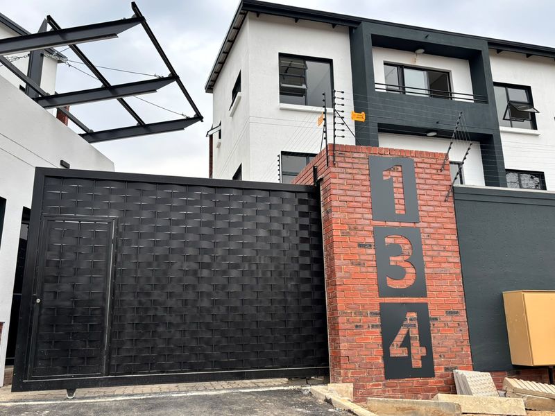 Modern apartment complex entrance featuring a secure sliding gate, brick pillar with house numbering, and integrated electric fencing.