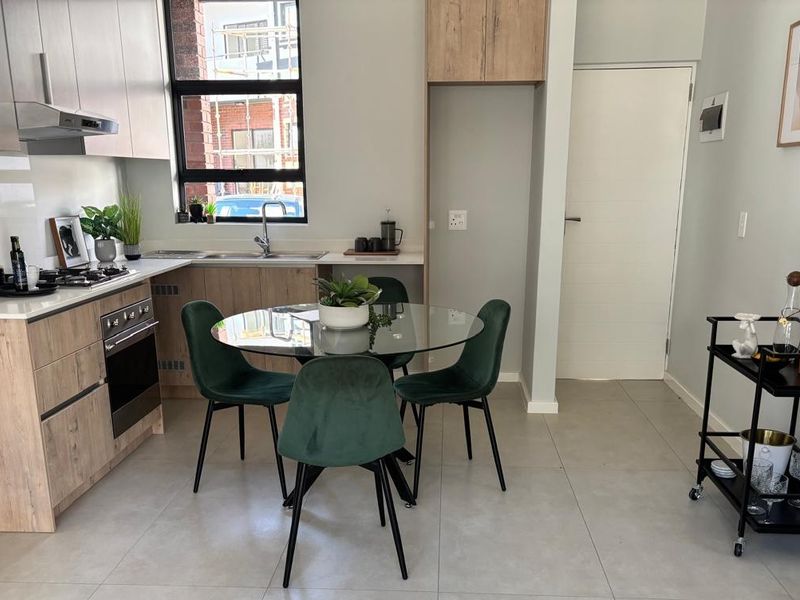 Modern open-plan kitchen and dining area featuring contemporary cabinetry, integrated appliances, and sleek tiled flooring in a well-maintained apartment setting.