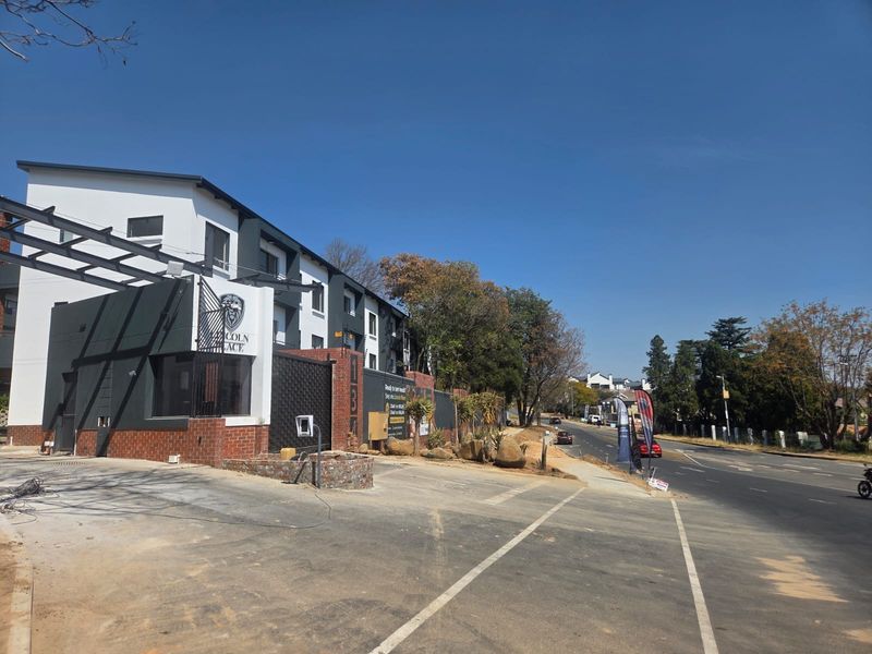 Front exterior view of the Lincoln Place apartment complex, featuring modern painted brick facade, secure gated entrance, and paved driveway area.
