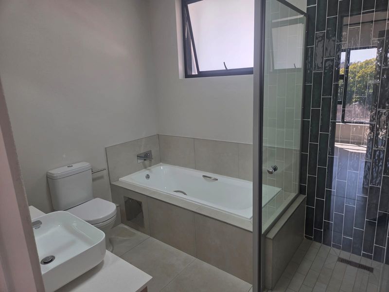 Modern bathroom featuring a built-in bathtub, separate glass-enclosed shower, wall-mounted basin, and contemporary tiled finishes.