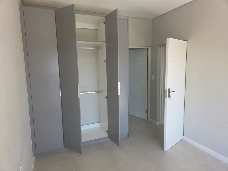 A clean, modern bedroom featuring neutral tiled flooring and ample built-in cupboard storage with a contemporary grey finish.