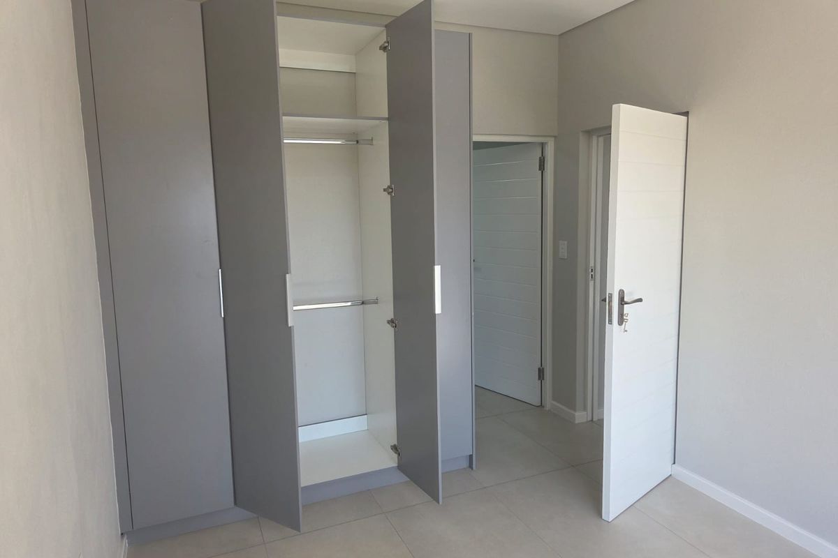 A clean, modern bedroom featuring neutral tiled flooring and ample built-in cupboard storage with a contemporary grey finish.