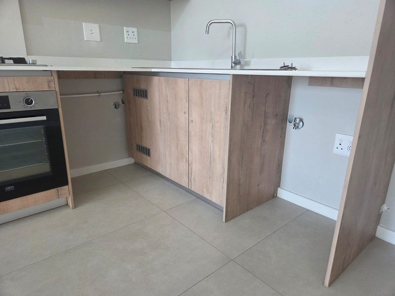 Modern kitchen area featuring light wood-look cabinetry, stone countertops, a built-in oven, and tiled flooring, with space prepared for additional appliances.