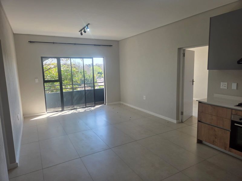 Modern open-plan living area featuring large format floor tiles, track lighting, and a sleek kitchen with built-in oven and stone countertops.