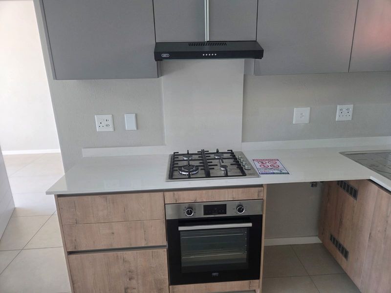 Modern kitchen featuring light wood-finish cabinetry, white quartz countertops, a built-in gas hob, oven, and extractor fan.