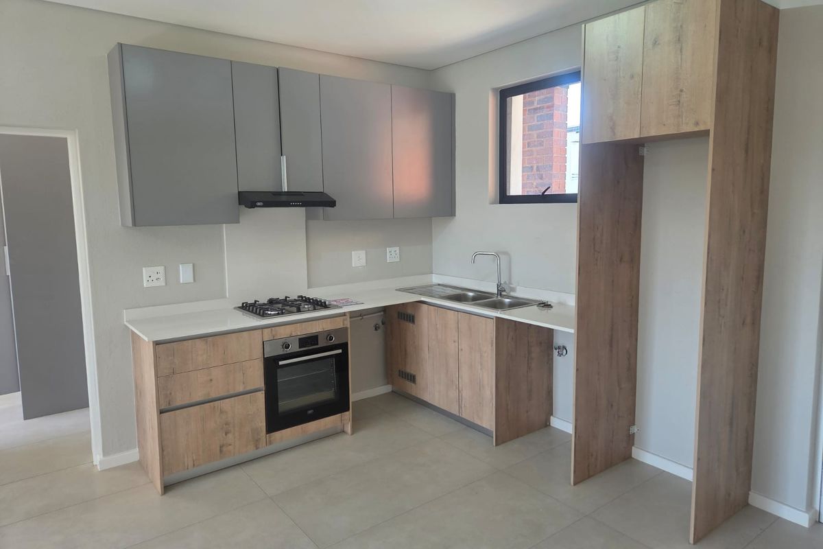 Modern kitchen featuring wood-look and grey cabinetry, stone countertops, integrated gas hob, electric oven, extractor fan, and a double sink with mixer tap.