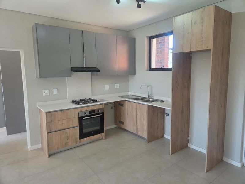 Modern kitchen featuring wood-look and grey cabinetry, stone countertops, integrated gas hob, electric oven, extractor fan, and a double sink with mixer tap.