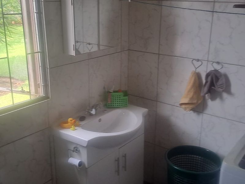 A functional laundry area featuring tiled walls, a vanity basin, and plumbing connections for a washing machine, with natural light from a side window.