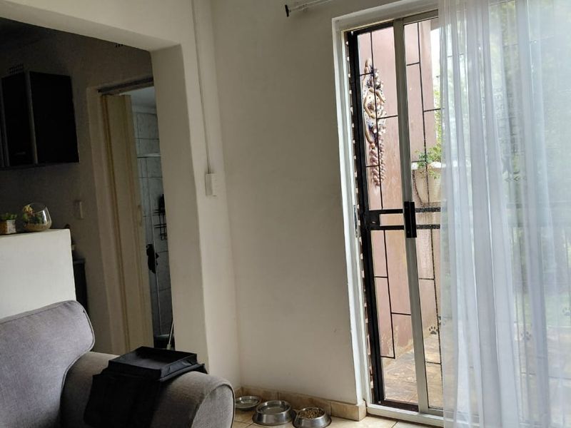 A living area featuring tiled flooring, ceiling cornicing, and a sliding glass door with a security gate providing access to the exterior.