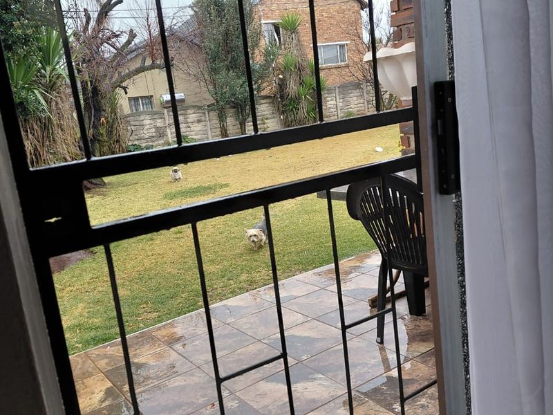A covered patio area featuring tiled flooring and a security gate, overlooking a private garden space.