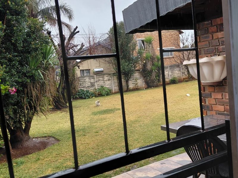 A covered patio area with tiled flooring and brick wall, overlooking a private garden space.