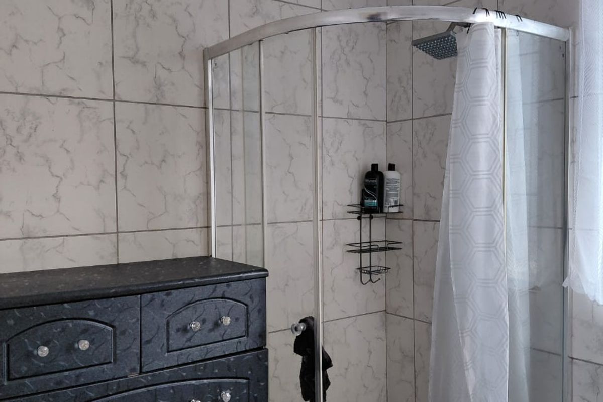 A functional bathroom featuring a corner shower enclosure with marble-look wall tiling and standard plumbing fixtures.