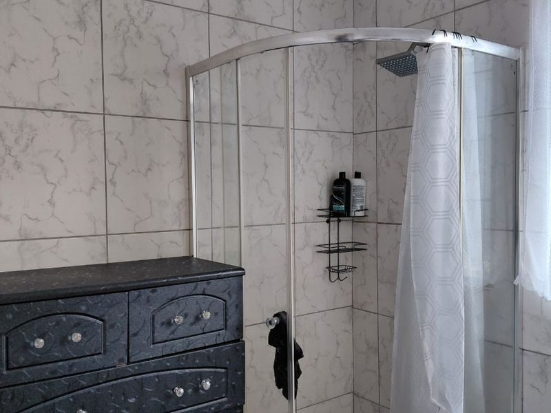 A functional bathroom featuring a corner shower enclosure with marble-look wall tiling and standard plumbing fixtures.