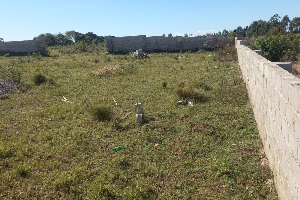 A vacant residential plot featuring established concrete block perimeter walls and natural grass coverage, ready for development.