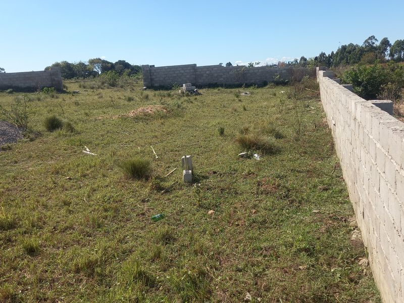 A vacant residential plot featuring established concrete block perimeter walls and natural grass coverage, ready for development.