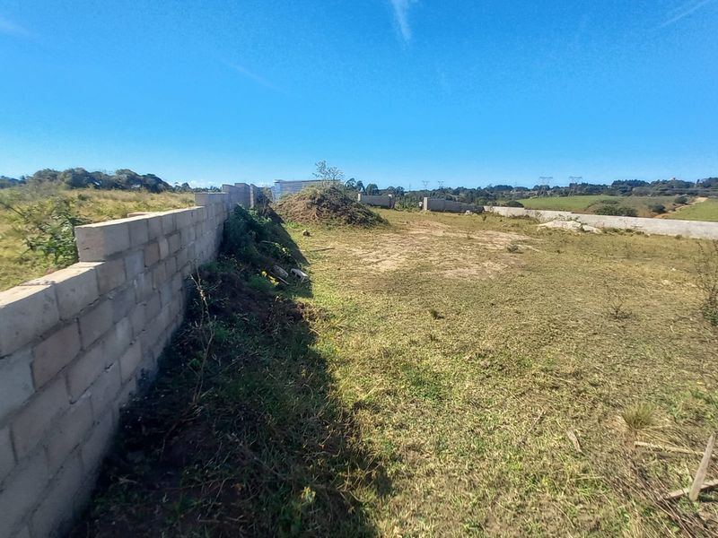 A vacant residential plot featuring a partially constructed concrete block boundary wall and open, undeveloped land with natural grass coverage.
