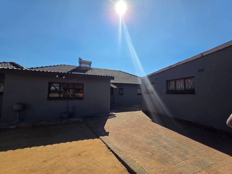 Rear exterior view of the property featuring a paved courtyard, tiled roof, and solar water heating system.