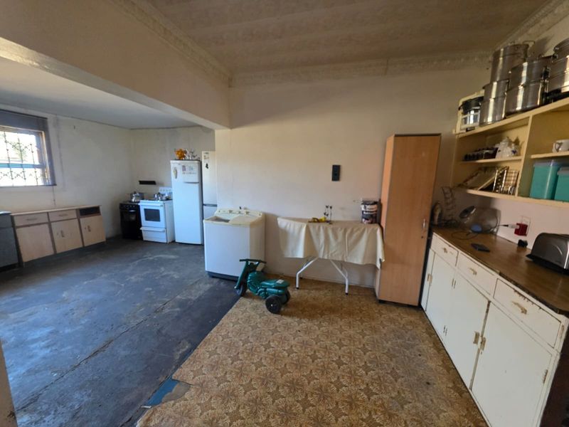 A spacious kitchen area featuring original cabinetry, open shelving, and a freestanding stove, requiring significant renovation and flooring updates to modernize the space.
