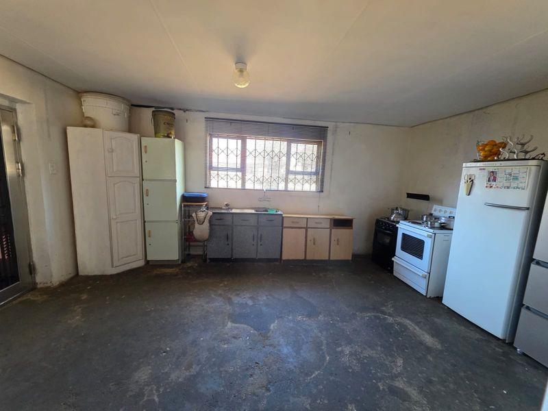 A dated kitchen area featuring basic cabinetry, a sink, and a stove, requiring significant renovation and modernization of finishes and flooring.
