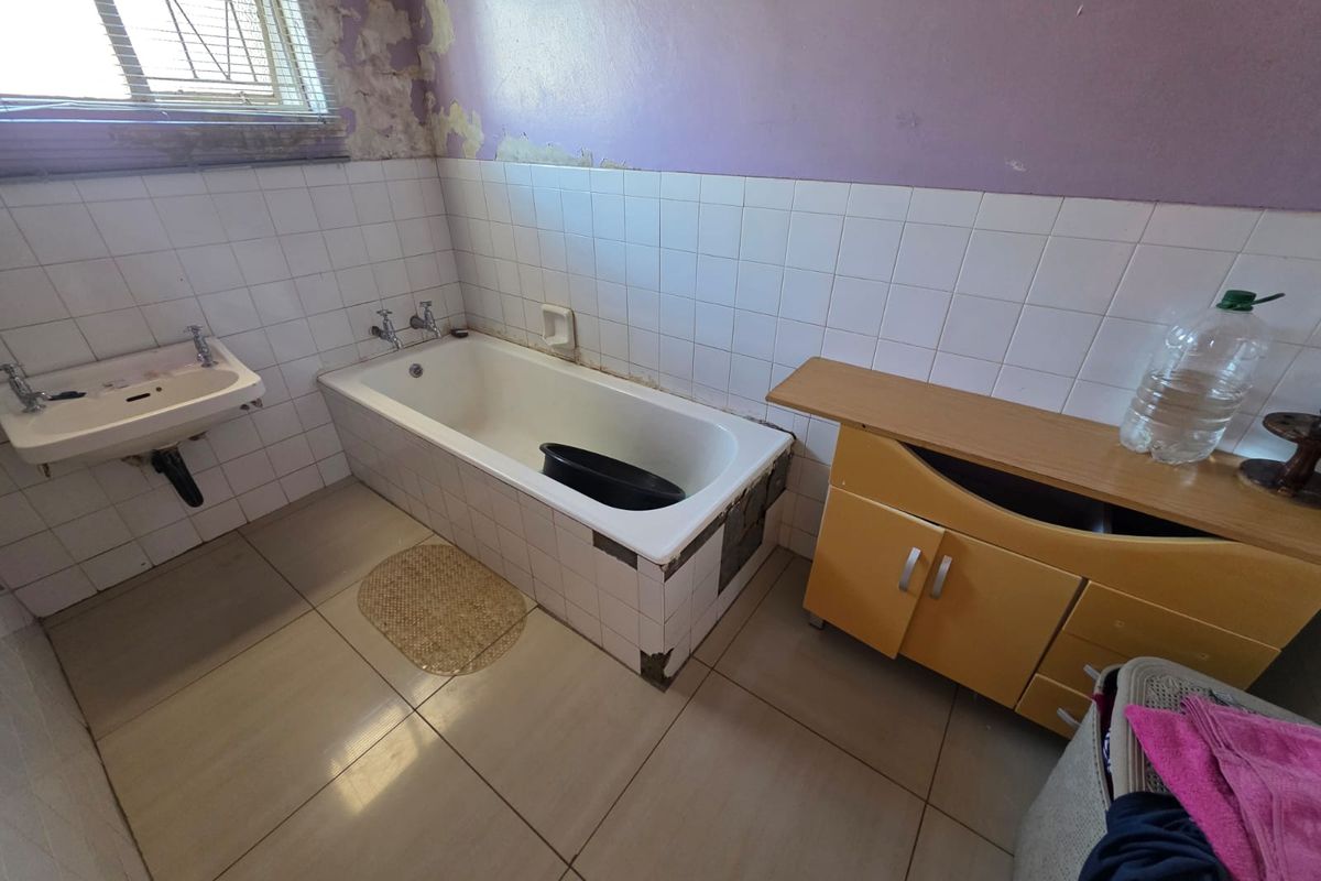 A dated bathroom featuring a bathtub, wall-mounted basin, and tiled surfaces, currently requiring significant cosmetic renovation and repair to the walls and tiling.