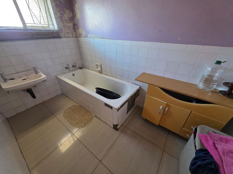 A dated bathroom featuring a bathtub, wall-mounted basin, and tiled surfaces, currently requiring significant cosmetic renovation and repair to the walls and tiling.