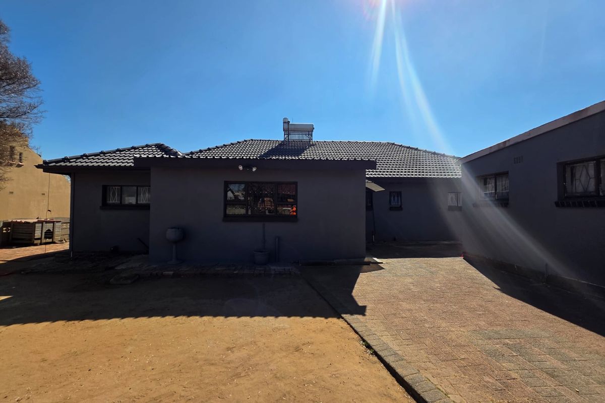 Rear view of the house featuring a tiled roof, solar geyser, security bars on windows, and a paved driveway leading to the building.