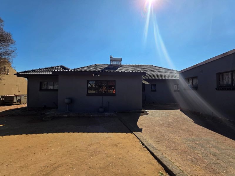 Rear view of the house featuring a tiled roof, solar geyser, security bars on windows, and a paved driveway leading to the building.