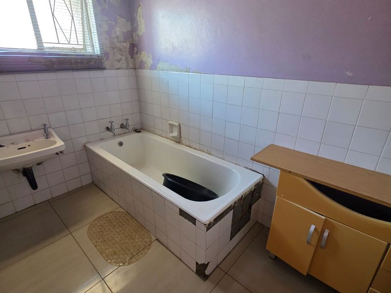A bathroom in need of renovation, featuring a built-in bathtub, wall-mounted basin, and vanity cabinet, with significant wall surface damage requiring repair.