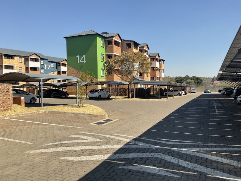 Exterior view of a multi-story apartment complex featuring paved parking areas with covered bays and established building facades.