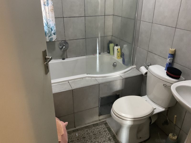 A functional bathroom featuring a bathtub with a glass screen, toilet, and washbasin, finished with neutral wall and floor tiling.