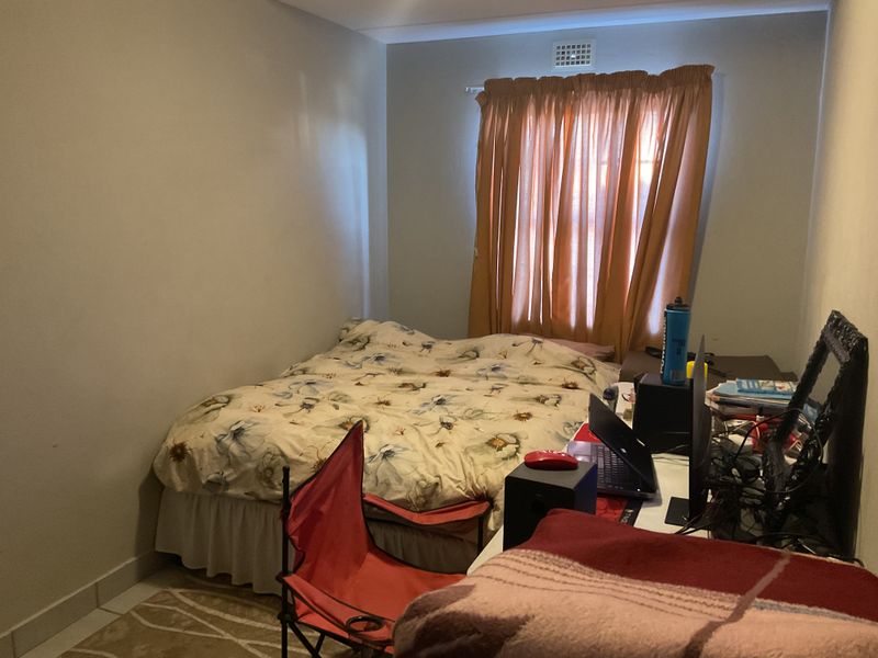 A standard bedroom featuring a window with curtains and a wall-mounted air vent.