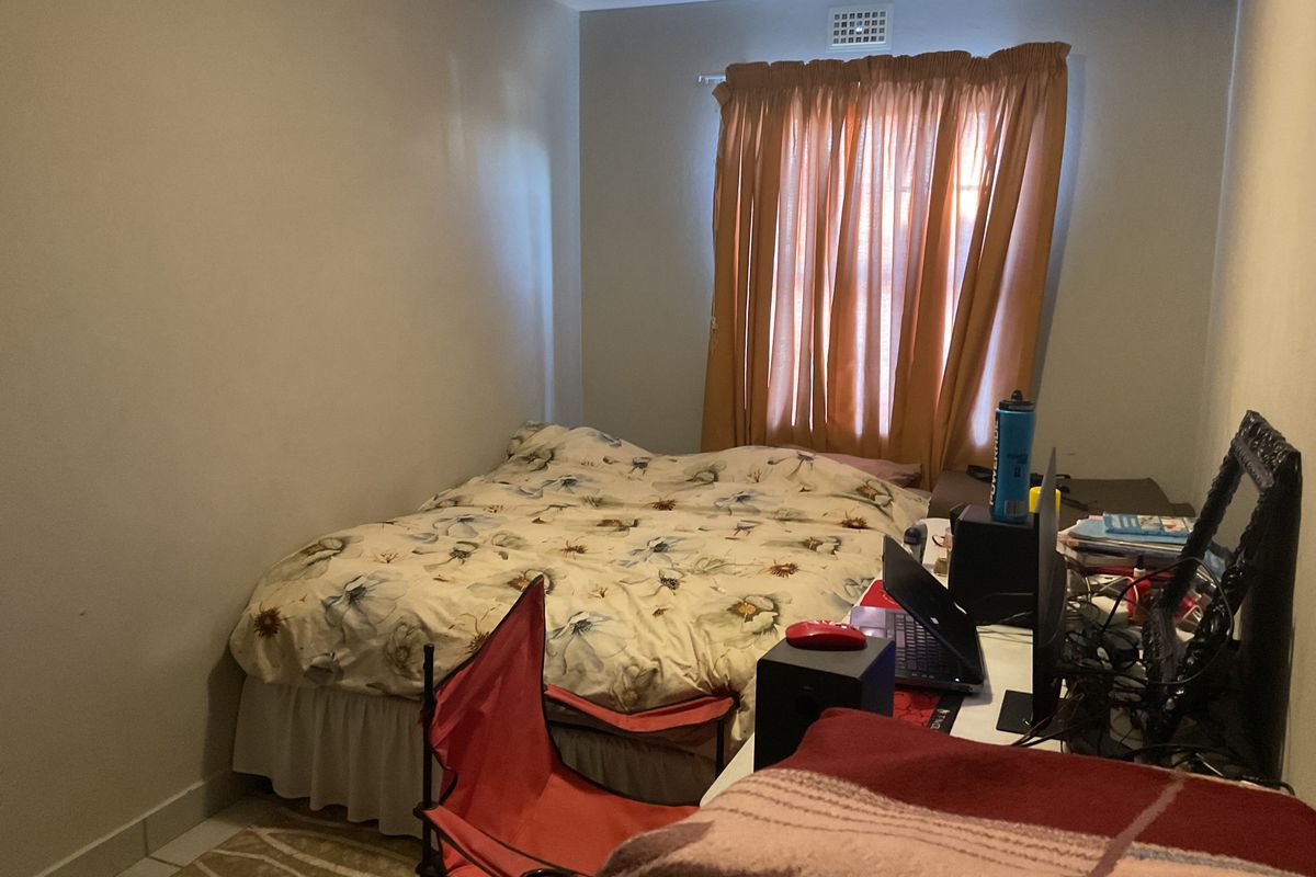 A standard bedroom featuring a window with curtains and a wall-mounted air vent.
