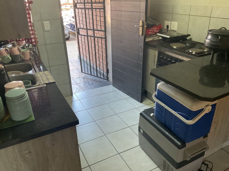 A functional kitchen featuring granite countertops, built-in cabinetry, and an electric hob, with direct access to an exterior security gate.