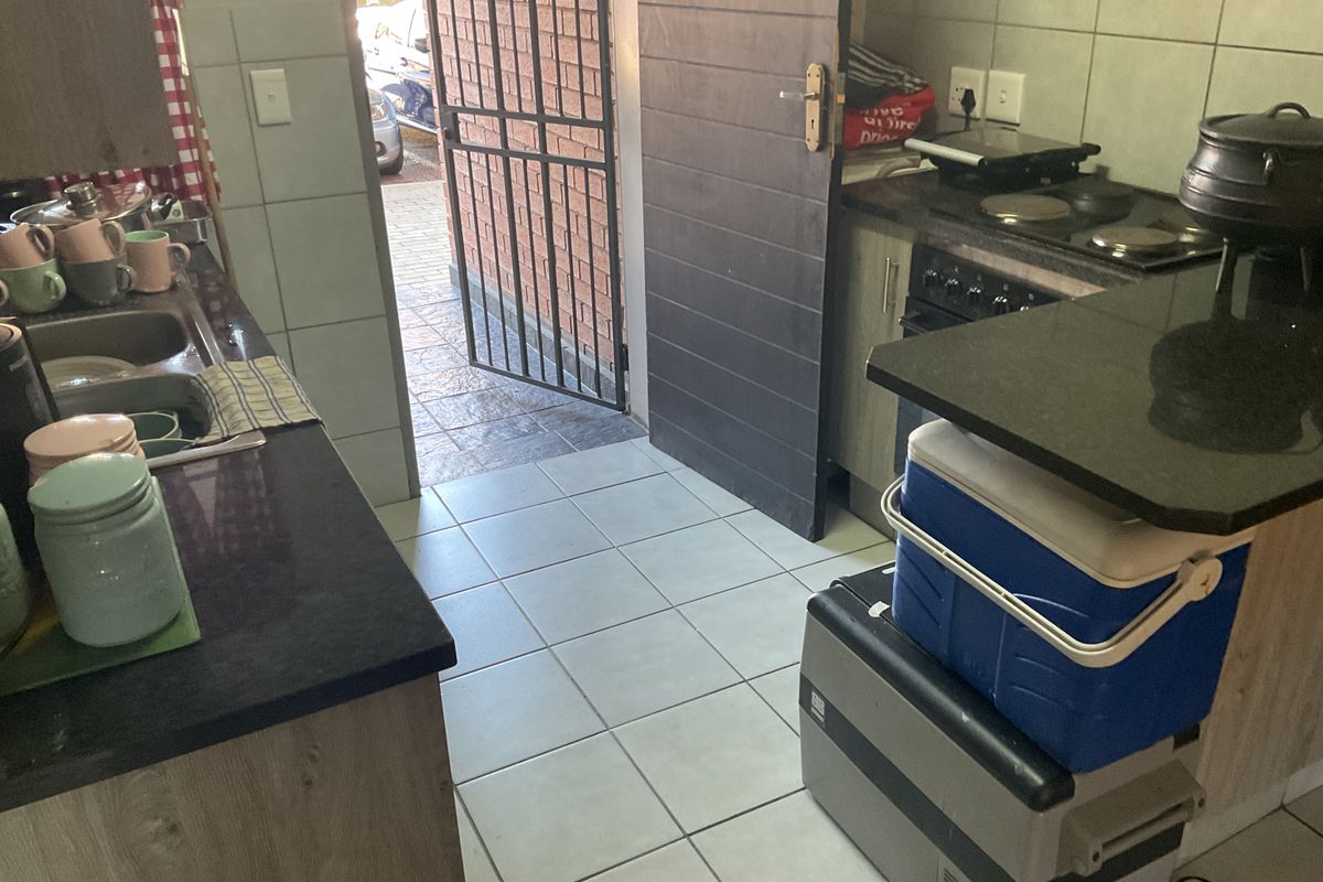 A functional kitchen featuring granite countertops, built-in cabinetry, and an electric hob, with direct access to an exterior security gate.