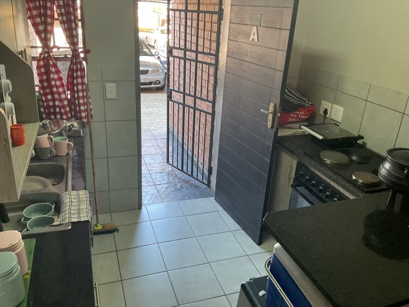Compact kitchen featuring built-in cabinetry, an electric stove, and direct access to the exterior through a security gate.