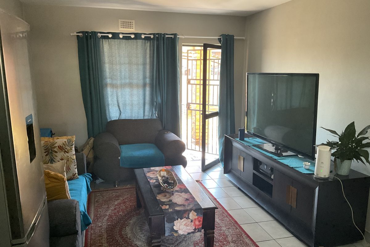 A functional living room featuring tiled flooring, a security gate leading to the exterior, and neutral wall finishes.