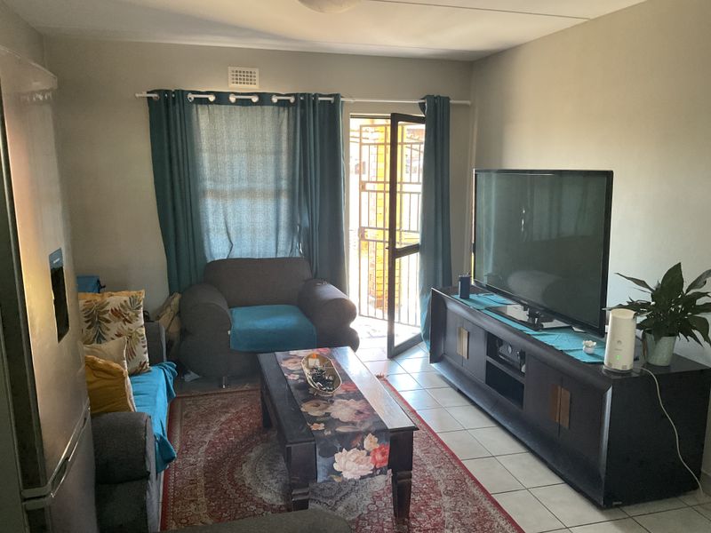 A functional living room featuring tiled flooring, a security gate leading to the exterior, and neutral wall finishes.