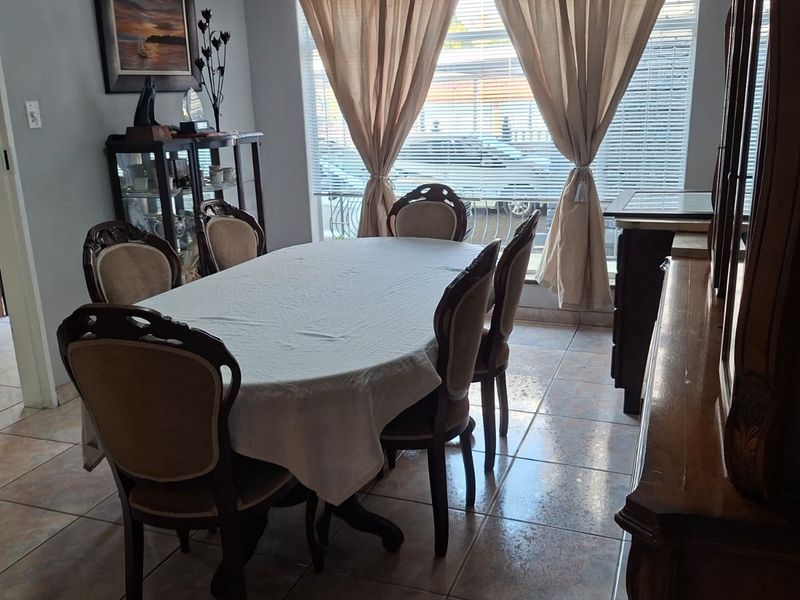 A dining room featuring tiled flooring, decorative cornicing, and large windows with venetian blinds, providing a functional space for family meals.