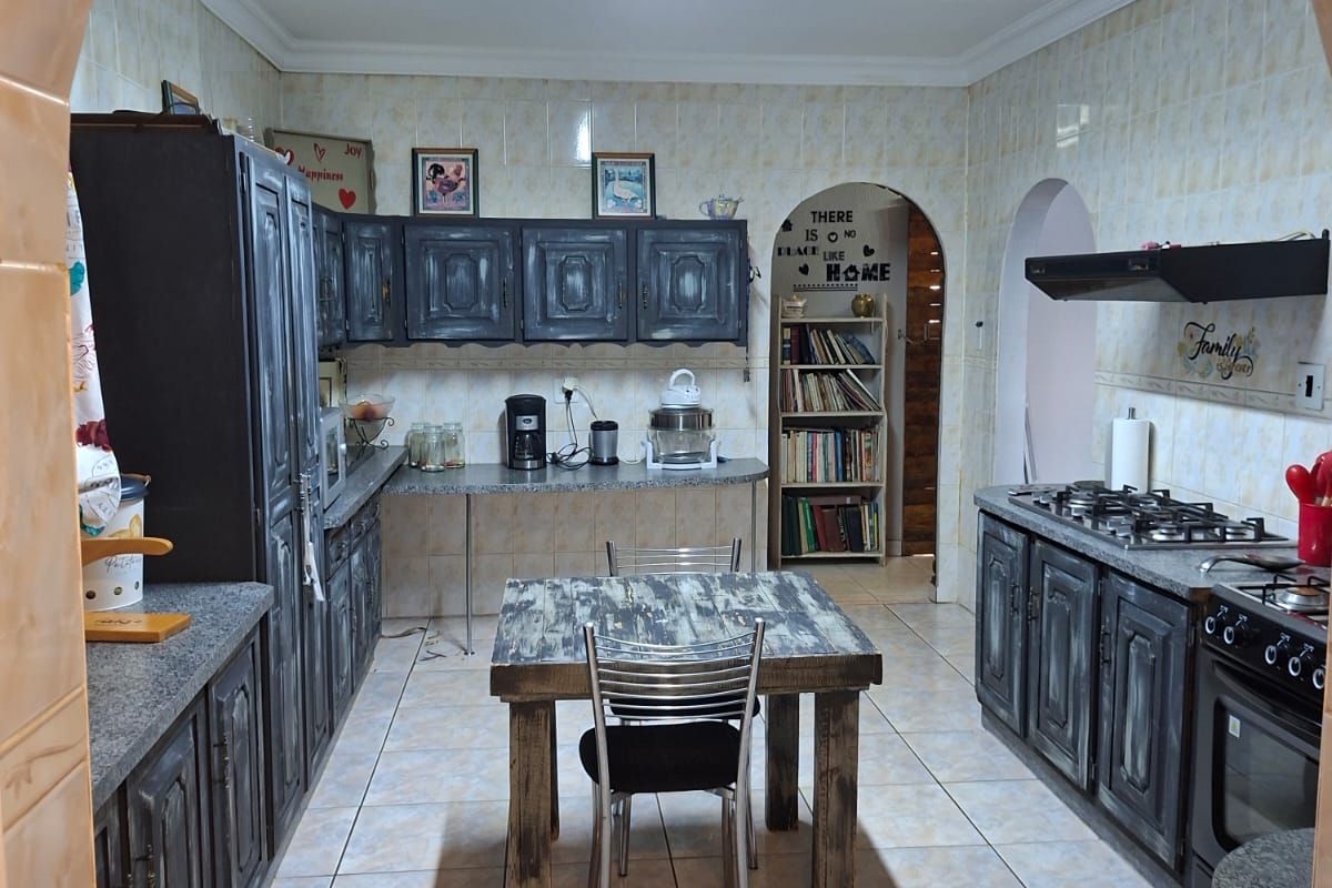 A functional kitchen featuring dark built-in cabinetry, a gas hob with extractor, tiled finishes, and a central dining area accessed through a classic archway.