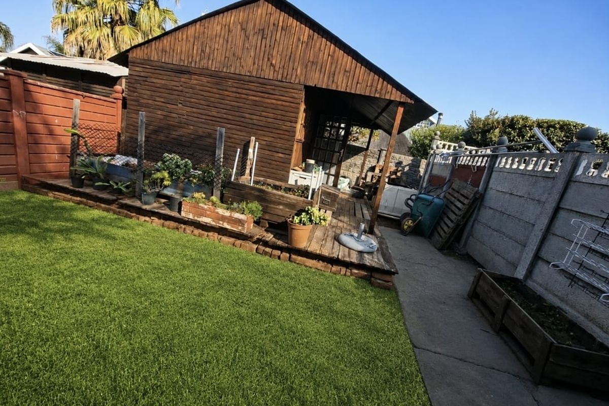 Rear garden area featuring a timber-clad structure with an attached wooden deck, concrete pathway, and perimeter boundary wall.