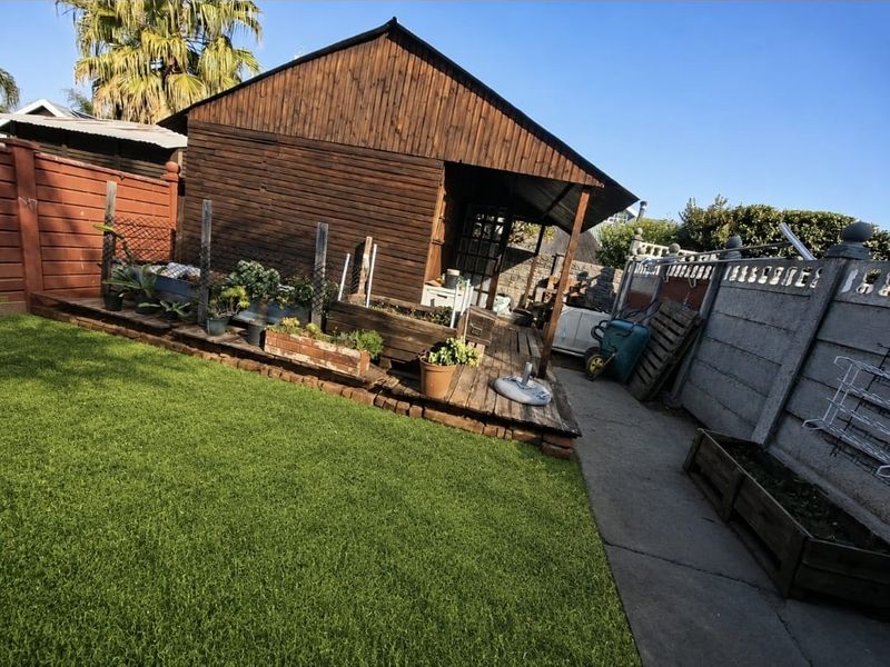 Rear garden area featuring a timber-clad structure with an attached wooden deck, concrete pathway, and perimeter boundary wall.