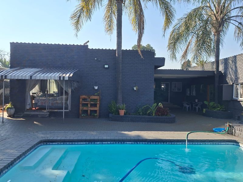 A rear exterior view featuring a swimming pool, paved patio area, and a dark-painted brick house facade with an awning.