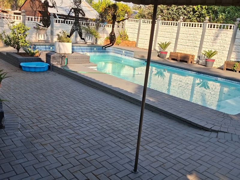 Outdoor pool area featuring a paved patio, covered entertainment space, and a swimming pool enclosed by a precast concrete boundary wall.