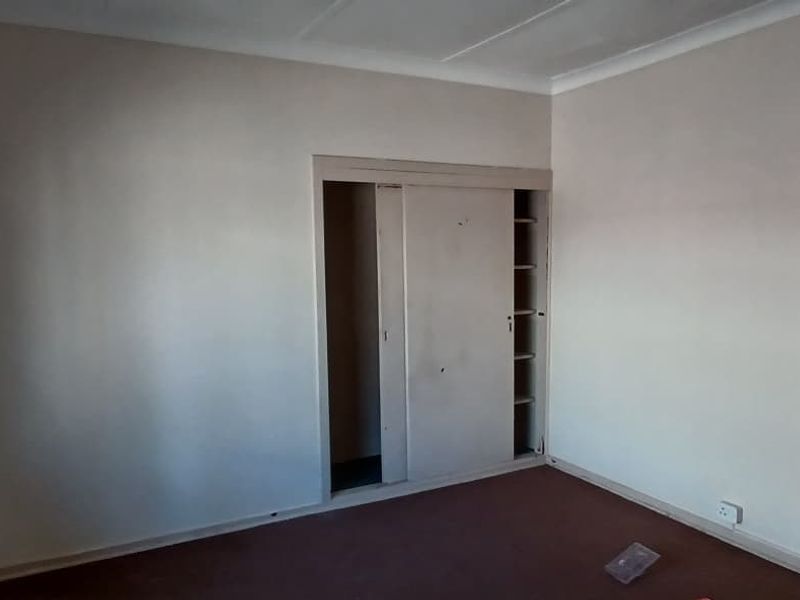 An empty bedroom featuring built-in sliding door wardrobes, cove cornicing, and carpet flooring, offering a blank canvas for renovation.