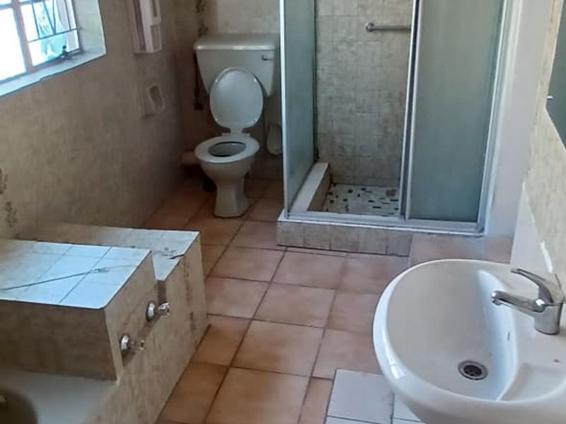 A dated bathroom featuring a pedestal basin, a built-in bathtub, a separate shower enclosure, and a toilet, with tiled walls and flooring throughout.