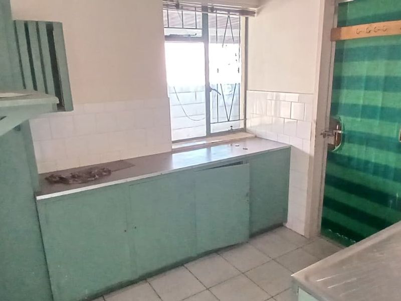 A dated kitchen featuring built-in cabinetry, a double stainless steel sink, and tiled splashbacks, requiring modernization to improve functionality and aesthetic appeal.