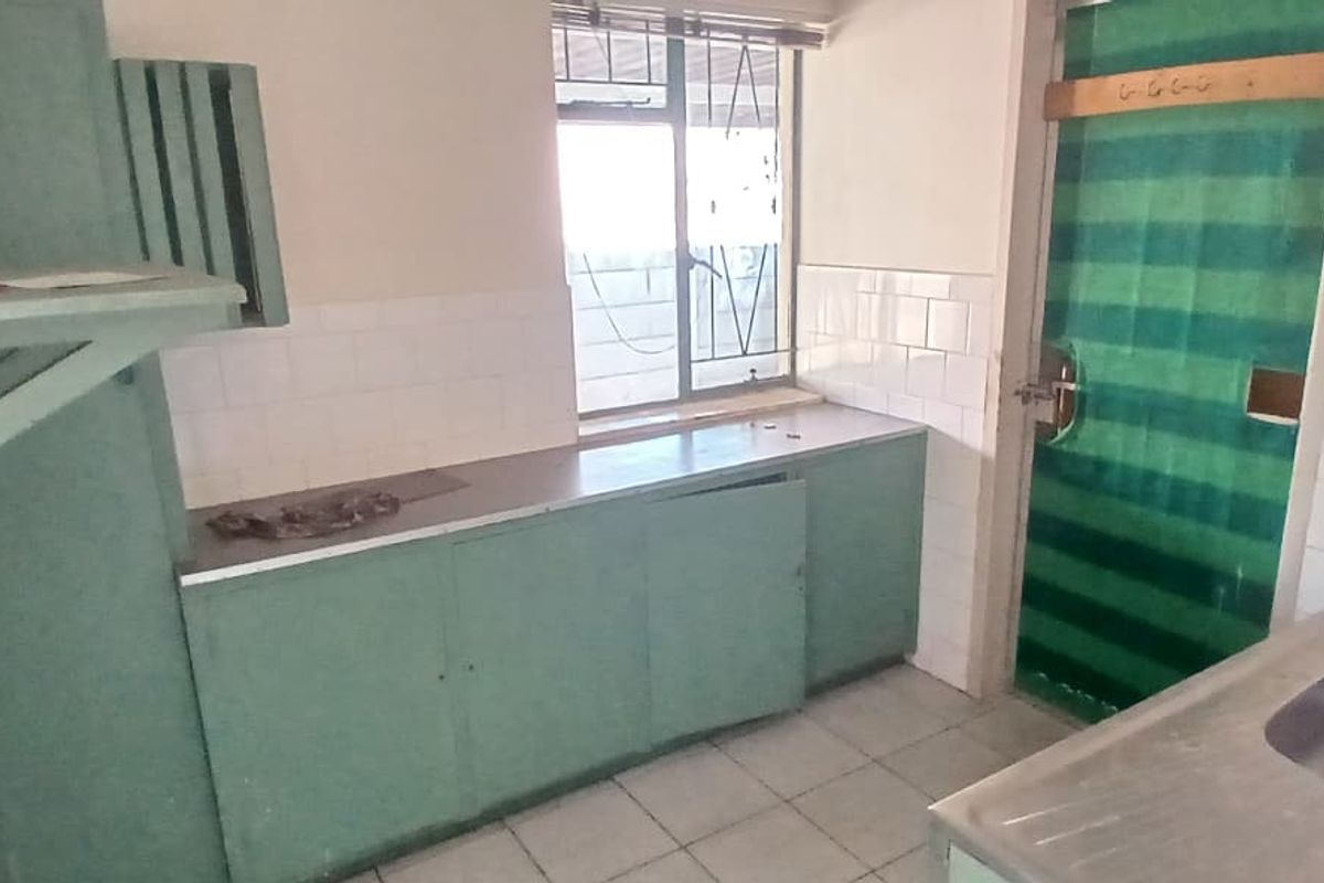 A dated kitchen featuring built-in cabinetry, a double stainless steel sink, and tiled splashbacks, requiring modernization to improve functionality and aesthetic appeal.