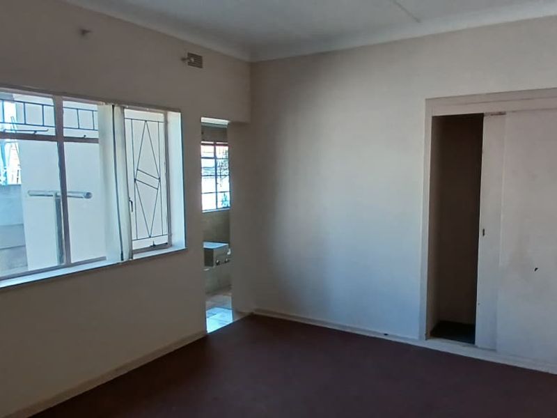An empty bedroom featuring built-in sliding door wardrobes, metal-framed windows with security bars, and carpeted flooring.