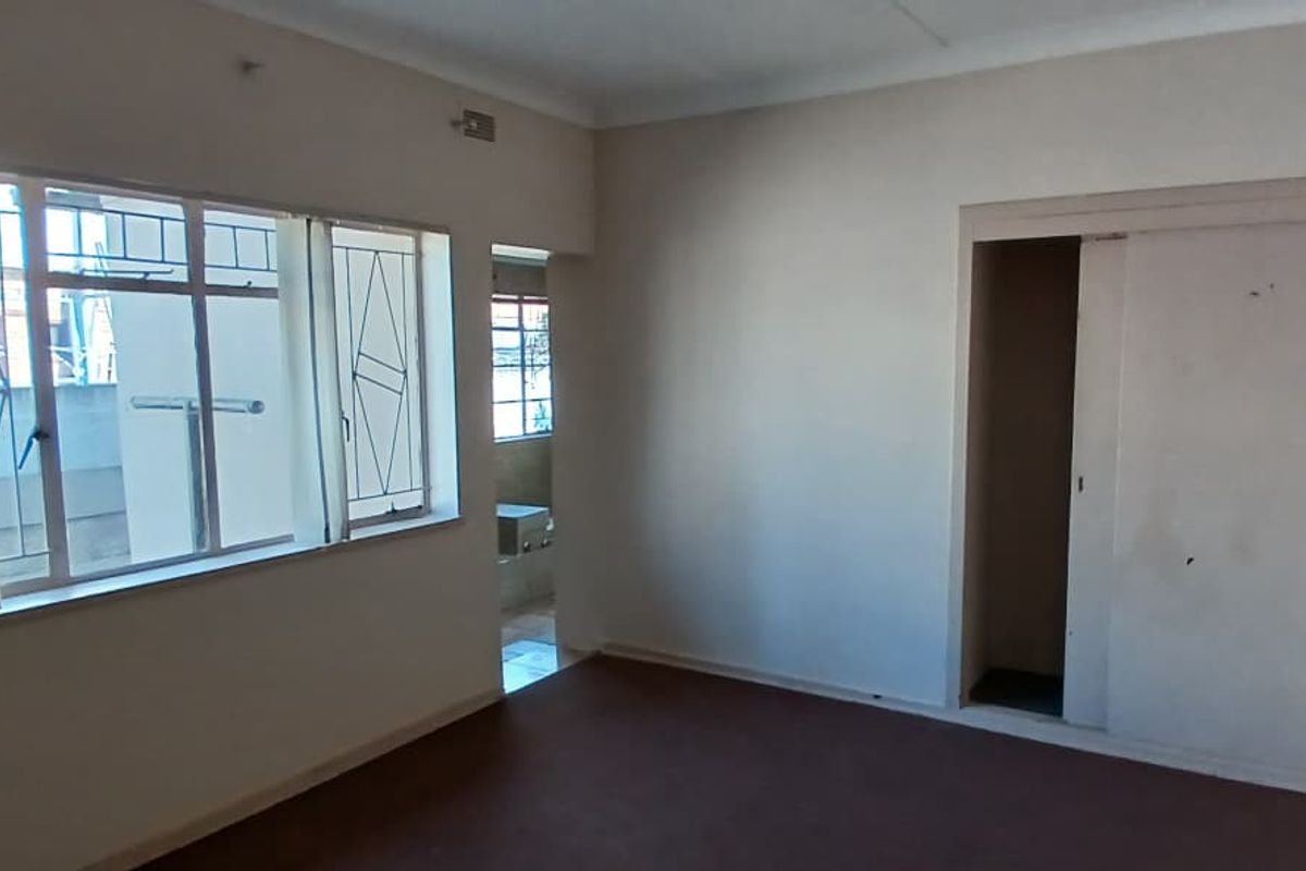 An empty bedroom featuring built-in sliding door wardrobes, metal-framed windows with security bars, and carpeted flooring.